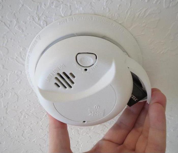 close view of hand opening battery door on a ceiling smoke alarm